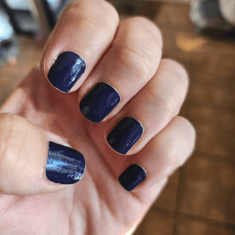 Deep navy blue nail wraps on hand showing glossy finish for DIY manicure