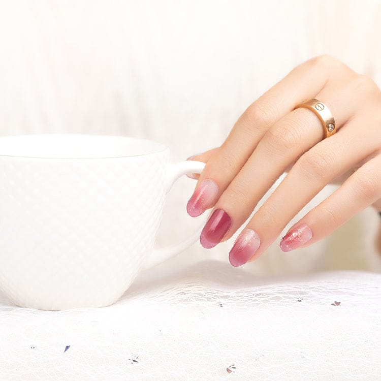 Pink shimmer nail wraps manicure on hand with wine glass