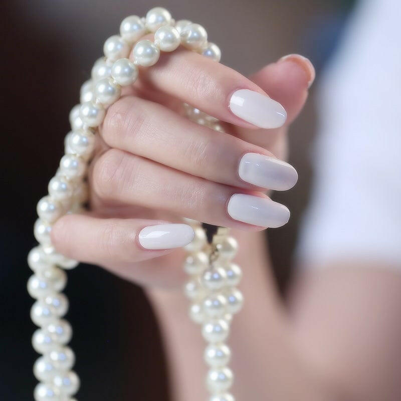 Light nude nail wraps on hand holding white pearl necklace showing elegant manicure