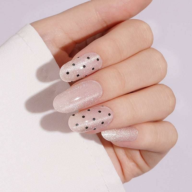 Shimmery nude pink press-on nails with black polka dot accents, almond shape