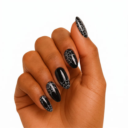 Glossy black almond press-on nails with white spiderweb Halloween design.