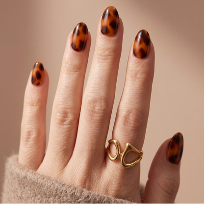 Glossy tortoiseshell nail wraps in amber and brown on almond-shaped press-on nails.
