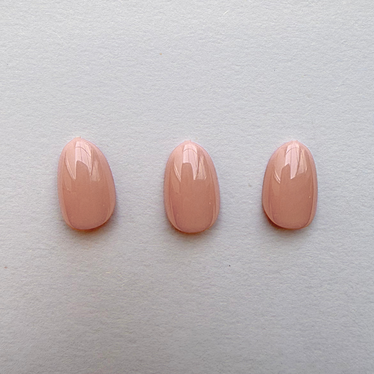 Glossy nude peach press-on nails in a solid, round-tip finish, three sizes shown