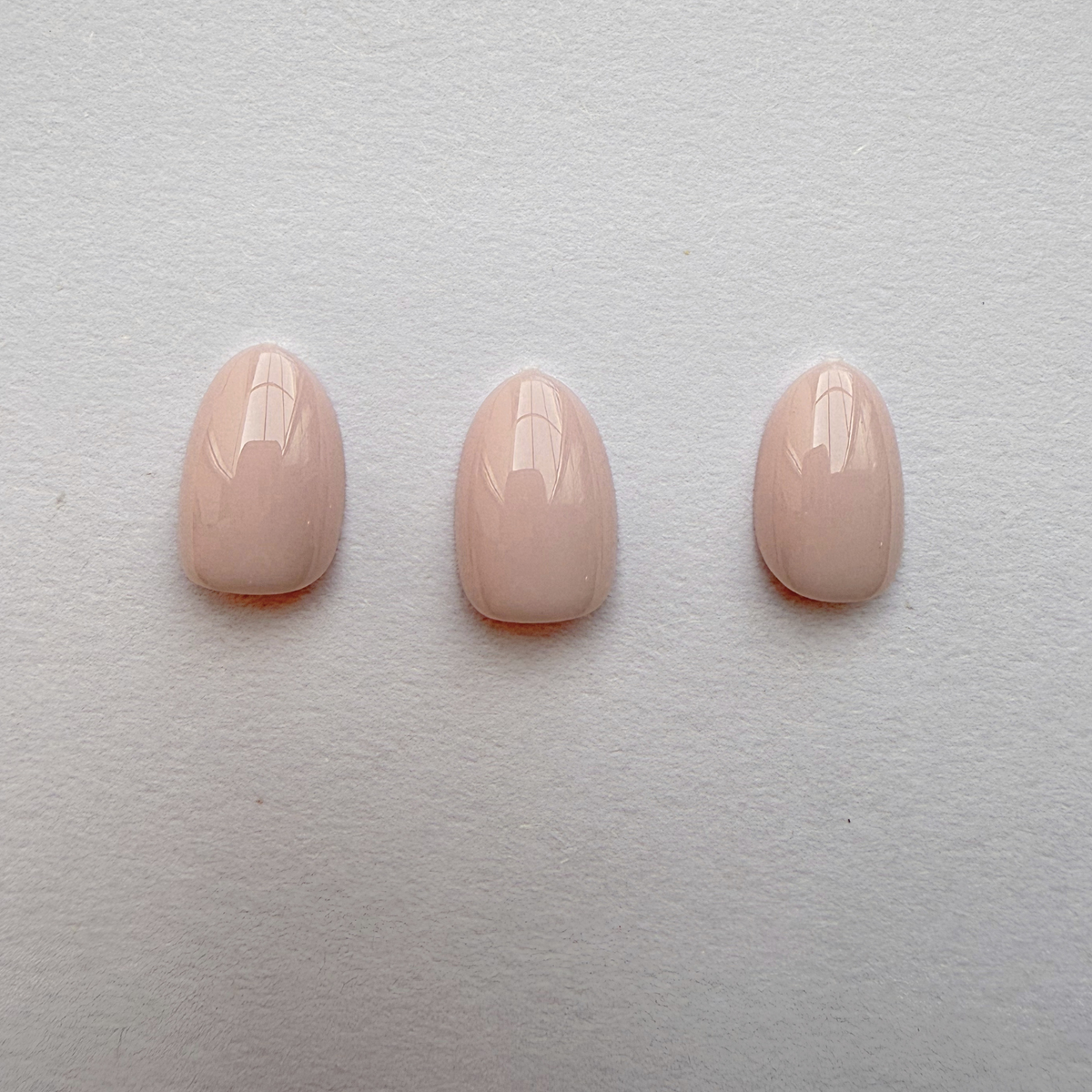 Solid nude pink glossy press-on nails, short round almond shape, set of three.