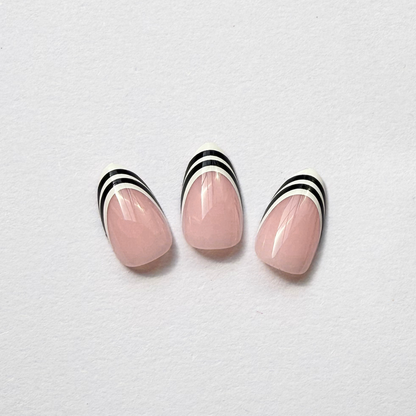 Glossy nude pink press-on nails with black and white striped French tips