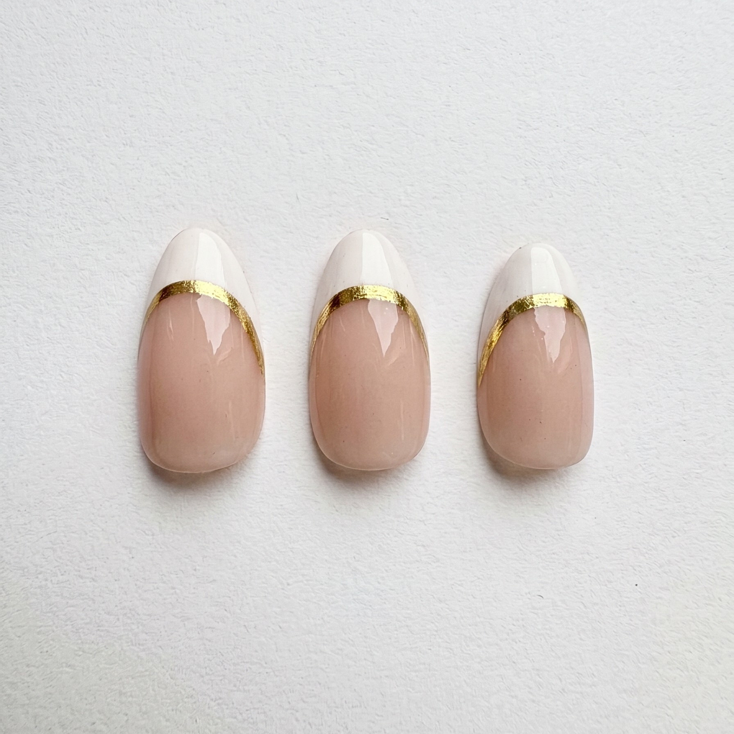 Glossy nude press-on nails with white French tips lined in gold foil