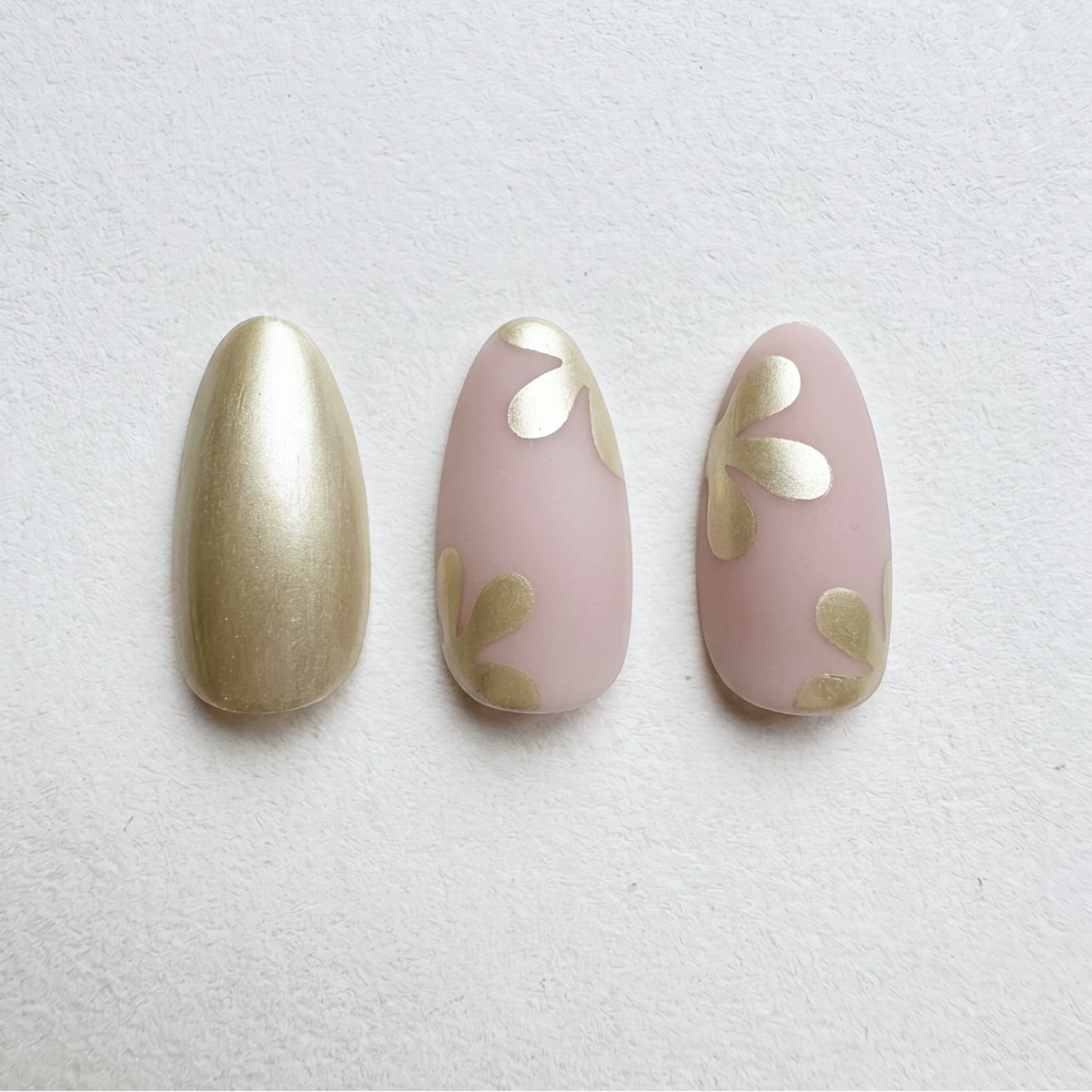 Press-on nails with metallic gold and matte pink shades, abstract floral petal accents.