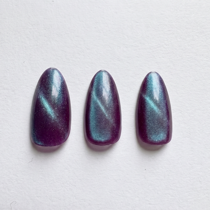 Deep purple press-on nails with shimmering teal-blue color-shifting cat-eye effect, almond shape.