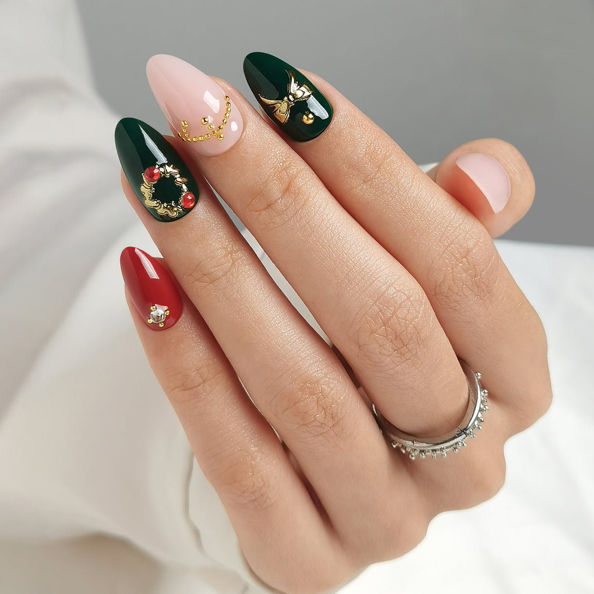 Green and red glossy press-on nails with gold wreath, bow, and bead charm accents