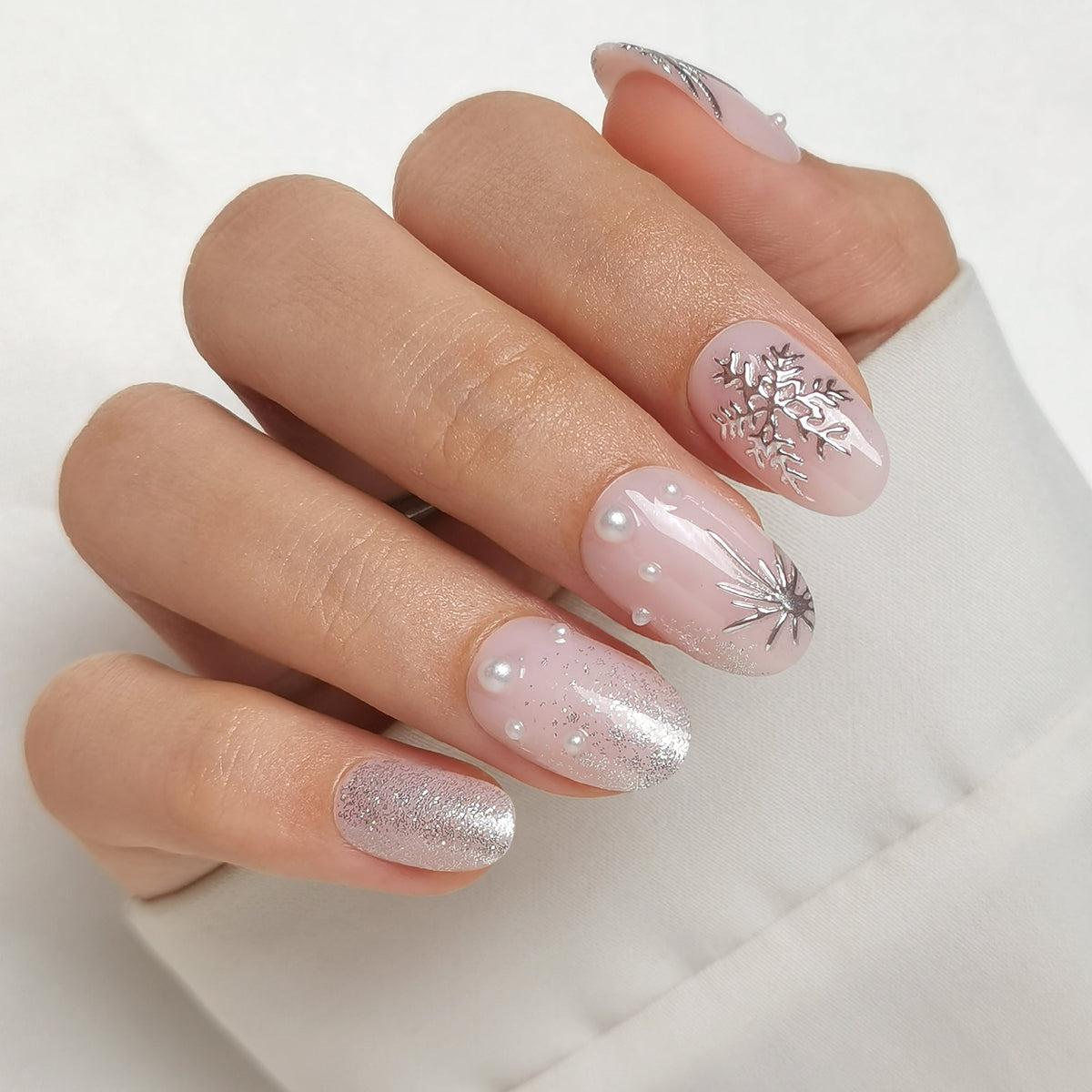 Sheer pink press-on nails with silver snowflakes, glitter, and pearl accents