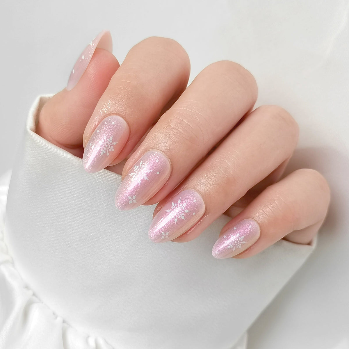 Shimmery pink almond press-on nails with white snowflake accents, soft gel finish