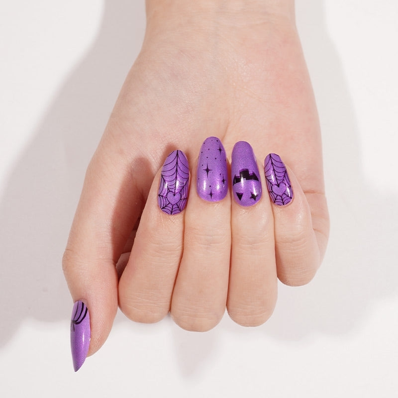 Purple shimmer nail wraps with black spiderweb, bat, and star Halloween designs