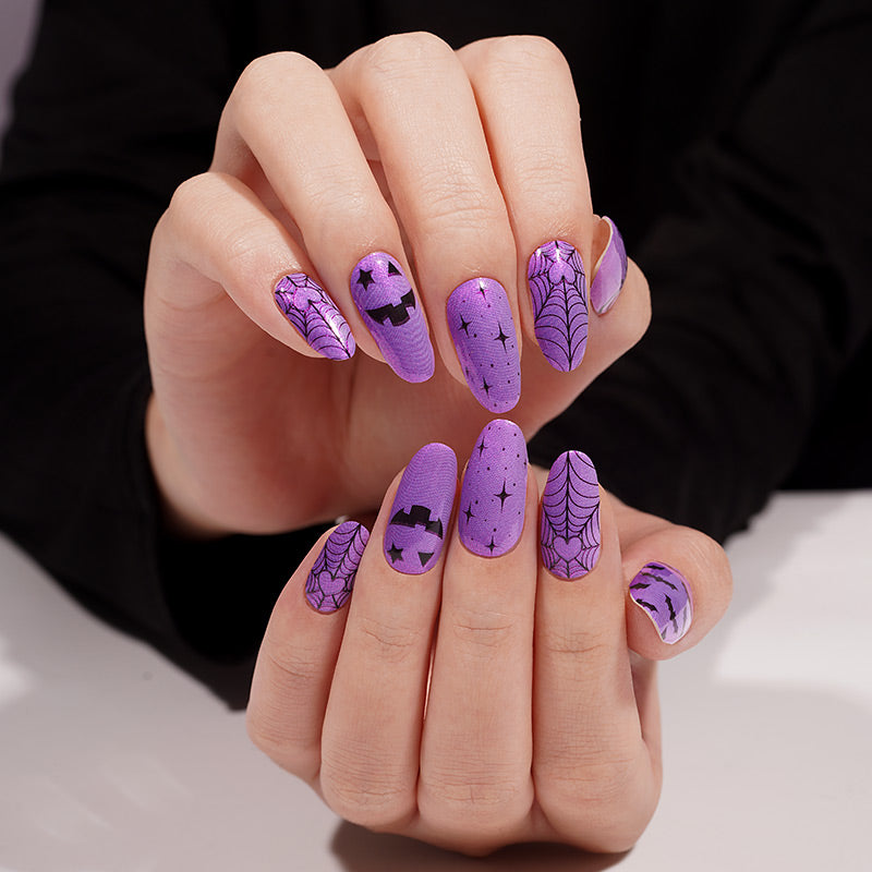 Purple shimmer press-on nails with black spiderweb, bat, and pumpkin Halloween designs.