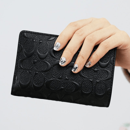 White and silver glitter butterfly nail wraps on hand holding black textured clutch bag