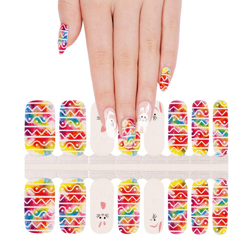 Hand showing festive Easter nail art with geometric rainbow stripes and cute white rabbit designs