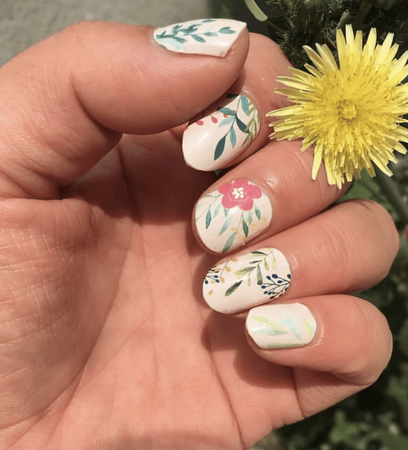Hand with yellow flower showing cream nail wraps featuring pink and green botanical floral motifs