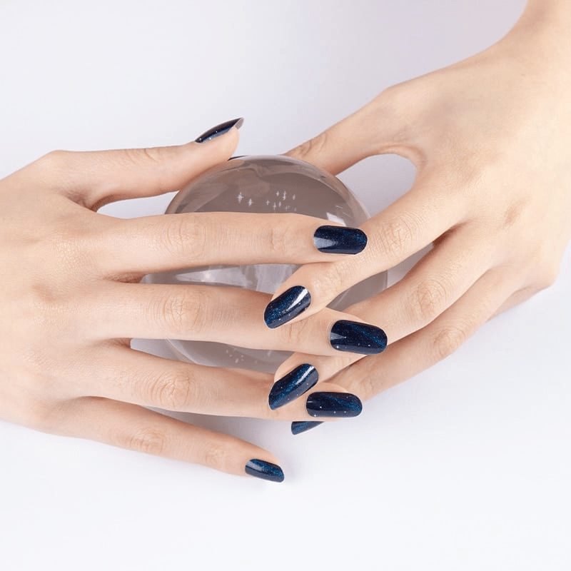 Hands displaying navy blue glossy nail wraps with crystal ball for celestial nail art