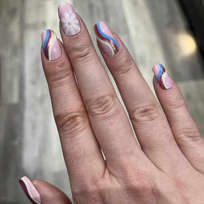 Hand wearing pink nail wraps with rainbow striped accent nails and daisy patterns