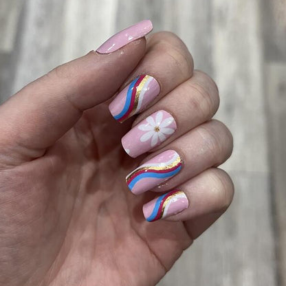 Hand displaying pink nail wraps featuring white daisy florals and colourful rainbow stripes