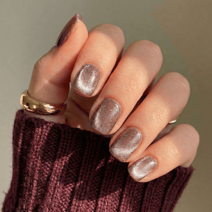 Rose gold cat's eye press-on nails with shimmer finish on hand wearing burgundy jumper
