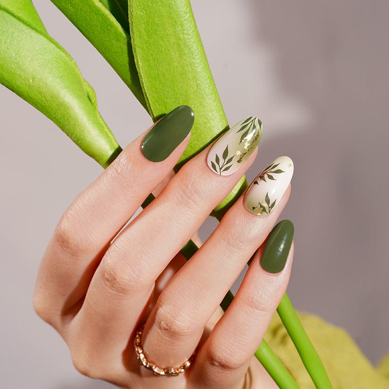 Green gel nail wraps with botanical leaf patterns on hand holding green plant stems